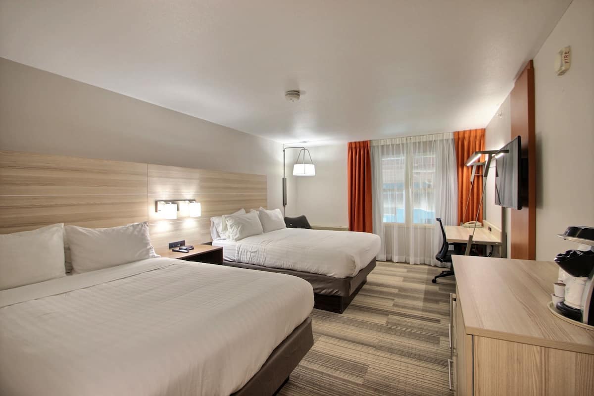 Ein Hotelzimmer mit zwei Betten, einem Schreibtisch, einem Fernseher und einer Lampe.
