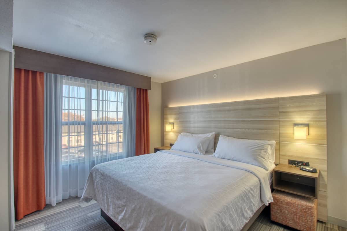 Ein Hotelzimmer mit einem großen Bett, zwei Nachttischen, einem Fenster mit Vorhängen.