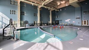 An indoor swimming pool with a blue tiled floor, a diving board, and a basketball hoop.