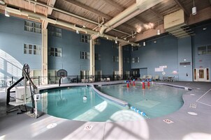 Una piscina interior con suelo de azulejos azules, un trampolín y un aro de baloncesto.