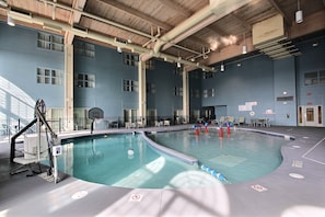 Una piscina interior con suelo de azulejos azules, un trampolín y un aro de baloncesto.