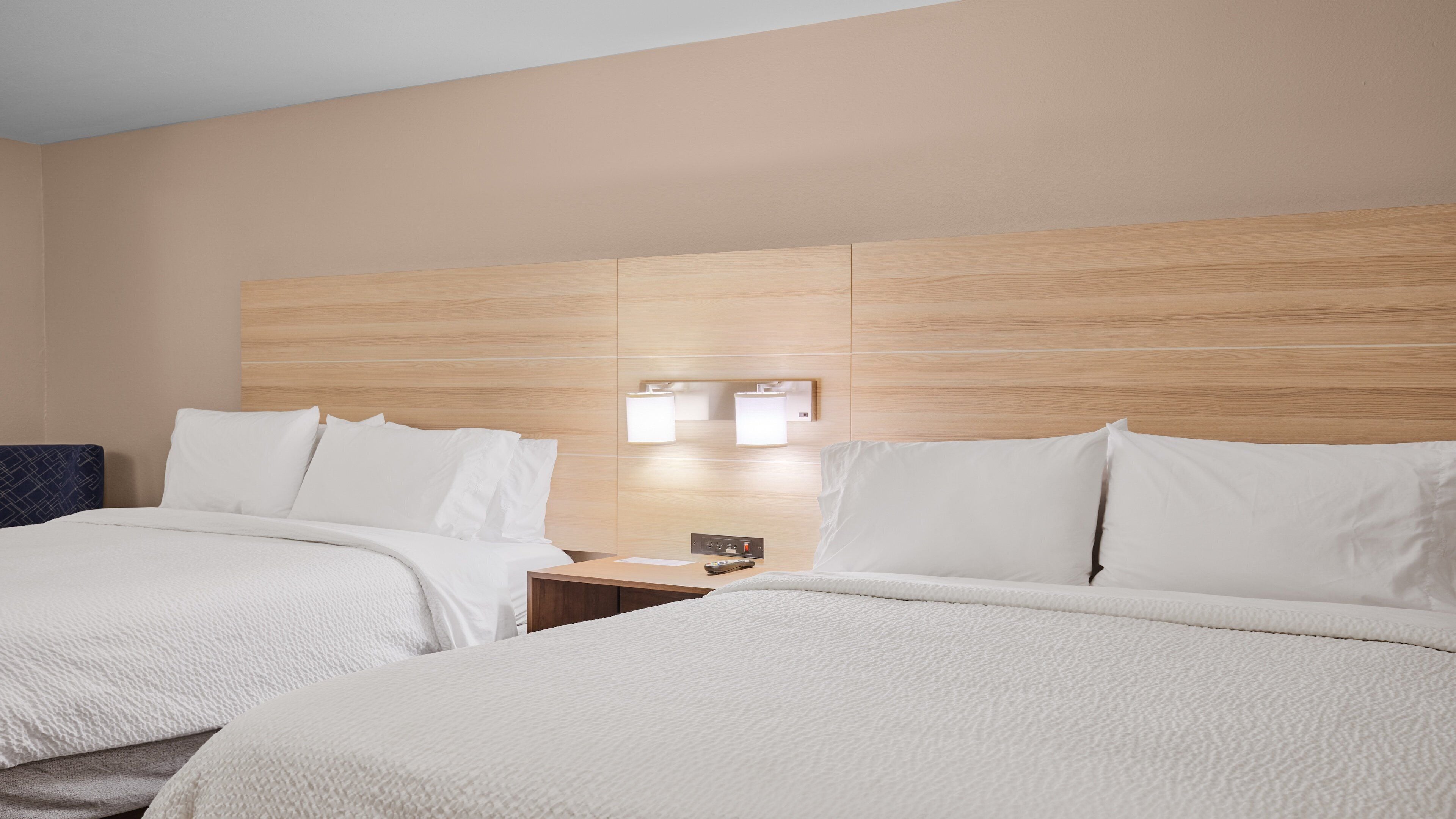 A hotel room with two beds, a wooden headboard, bedside tables, and wall-mounted lights.
