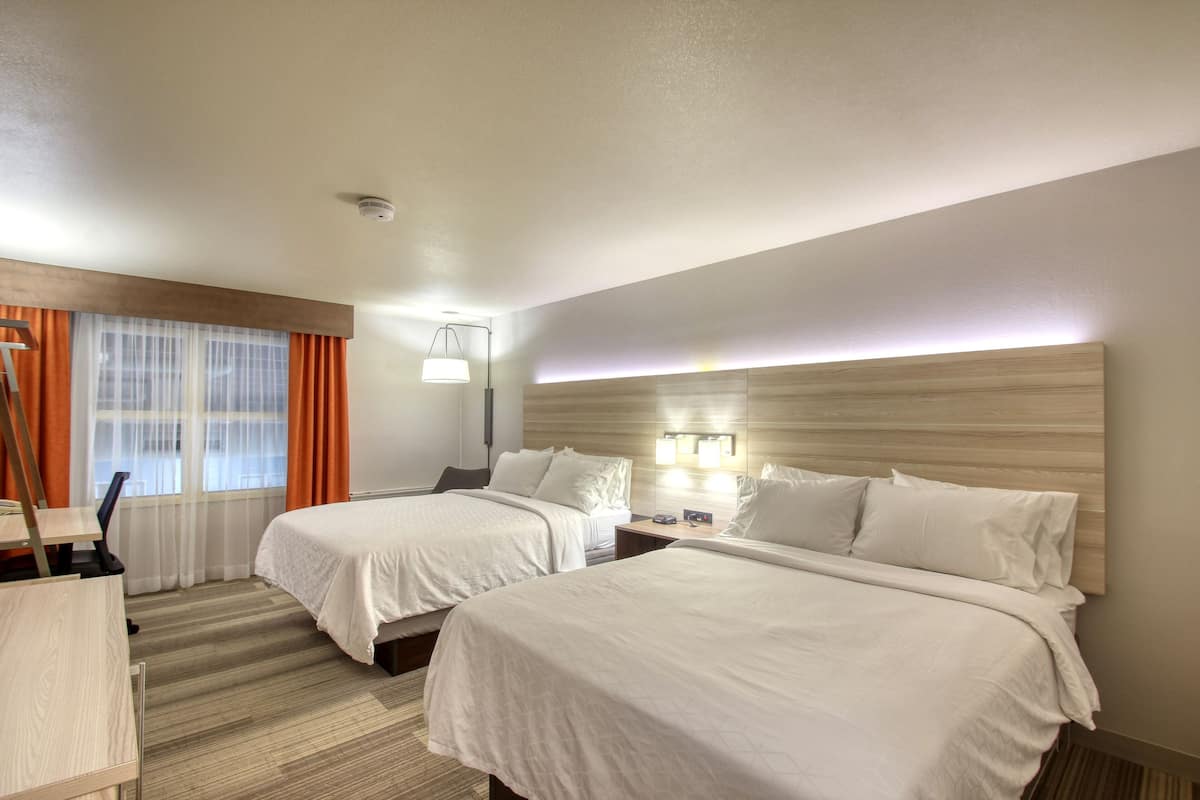 Ein Hotelzimmer mit zwei Betten, einem Schreibtisch, einem Stuhl, einer Lampe und einem Fenster mit Vorhängen.