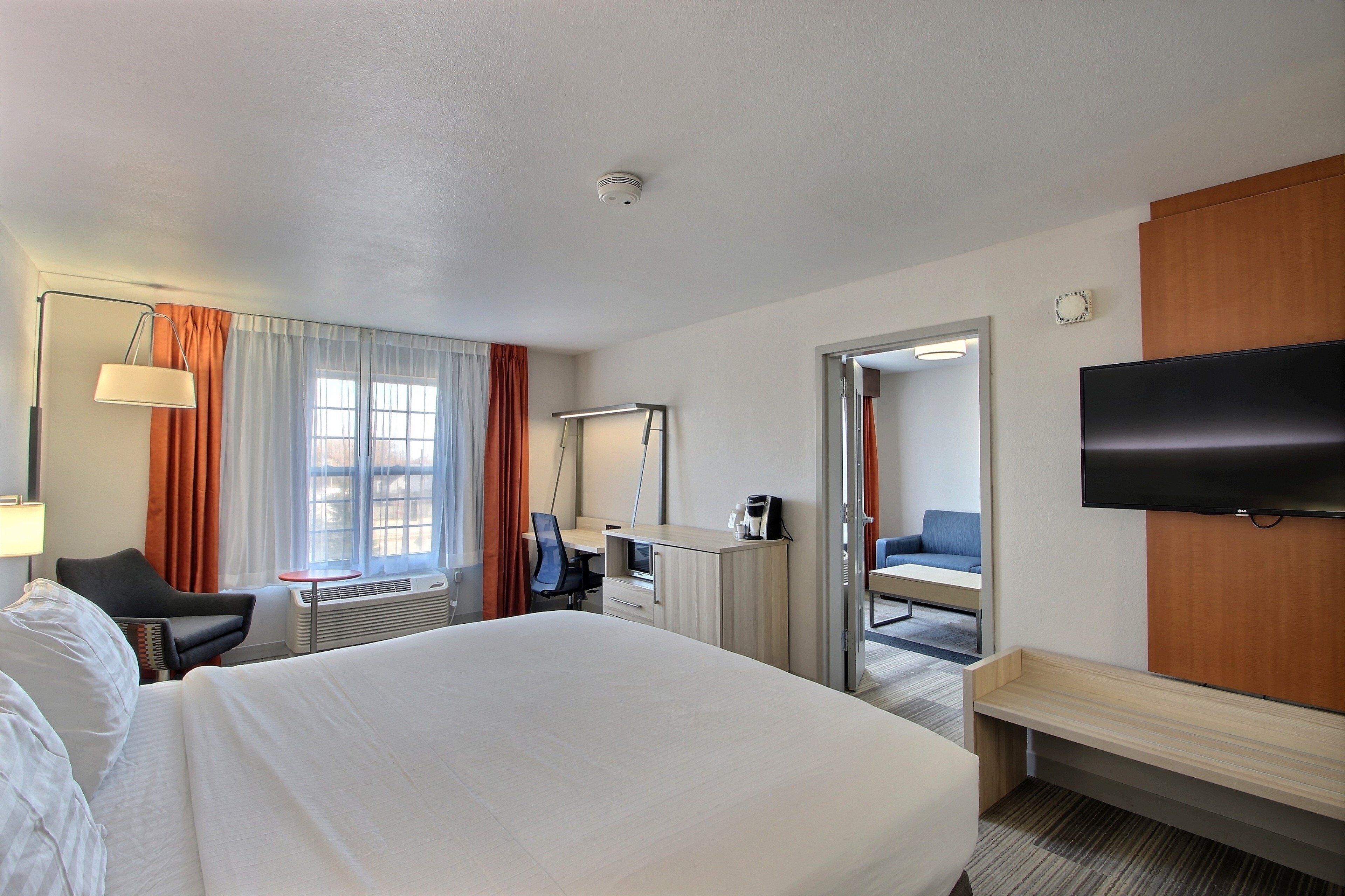 A hotel room with a bed, a desk, a chair, a TV, and a bathroom visible through an open door.