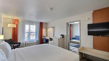 Quarto de hotel com cama, escrivaninha, cadeira, televisão e banheiro visível por uma porta aberta.