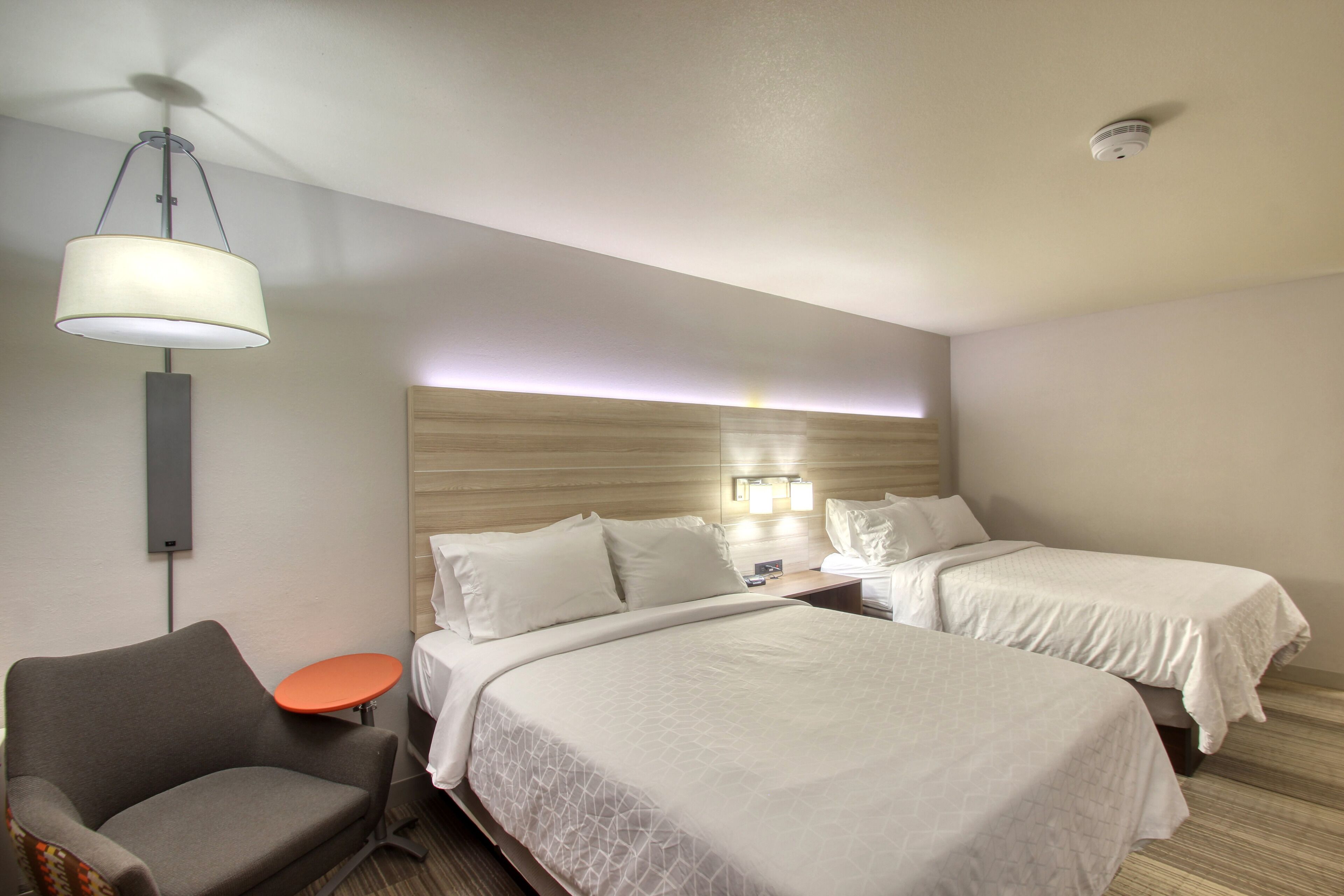 Una habitación de hotel con dos camas, una silla, una mesita y un ventilador de techo.