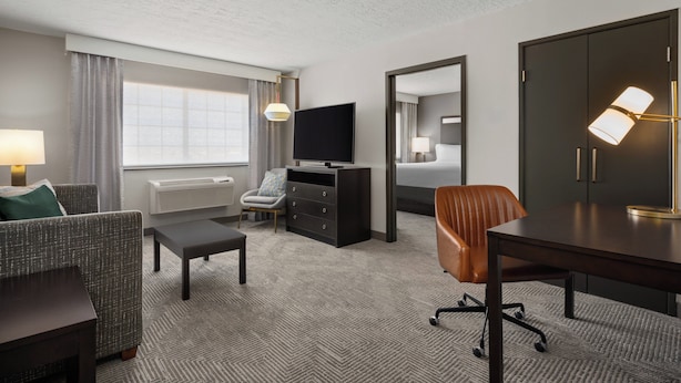 Quarto de hotel com sofá, escrivaninha, televisão, cômoda, espelho e armário.