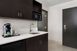 Cocina moderna con gabinetes oscuros, encimera blanca, microondas integrado, cafetera y pileta de acero inoxidable.