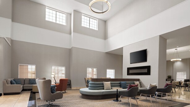 A spacious living area with a high ceiling, a large sectional sofa, multiple seating options, and a flat-screen TV mounted on the wall. - Holiday Inn & Suites Albuquerque Airport by IHG (Albuquerque)