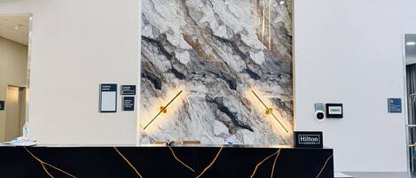 Un hall d’accueil moderne, avec un mur de marbre, un comptoir noir agrémenté de motifs dorés et une enseigne indiquant « Hilton Honors ».