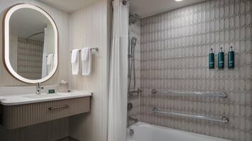 A modern bathroom with a vanity, a large mirror, a shower with a glass door, and toiletries on the wall.