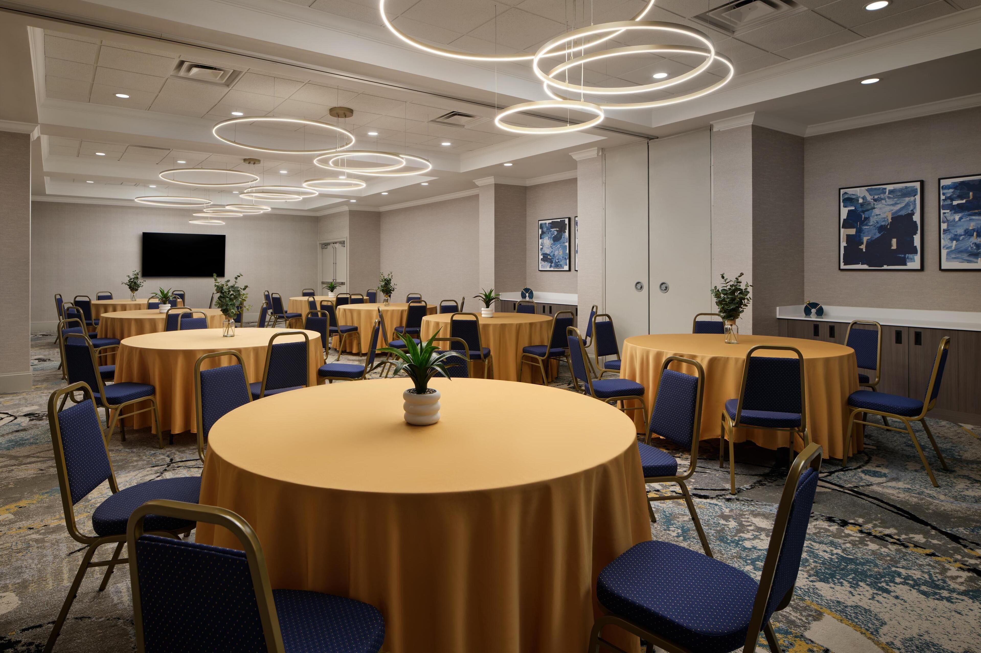A conference room with multiple round tables, blue chairs, and a modern ceiling design.