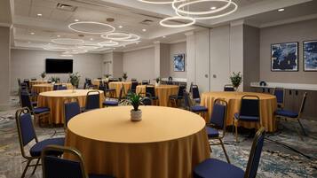 A conference room with multiple round tables, blue chairs, and a modern ceiling design.