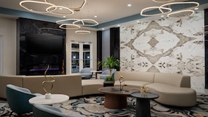 A modern living room with a sectional sofa, a flat-screen TV, and a decorative plant. - DoubleTree by Hilton Brunswick (Brunswick)