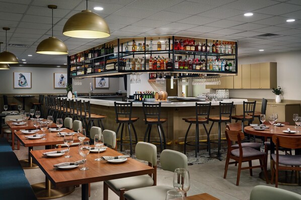 A restaurant with multiple dining tables, chairs, and a bar area with shelves of bottles.