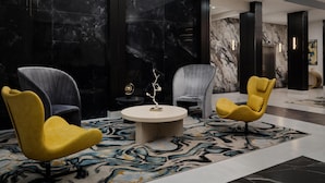 A modern lobby with marble walls, two yellow chairs, a round table, and a patterned carpet. - DoubleTree by Hilton Brunswick (Brunswick)
