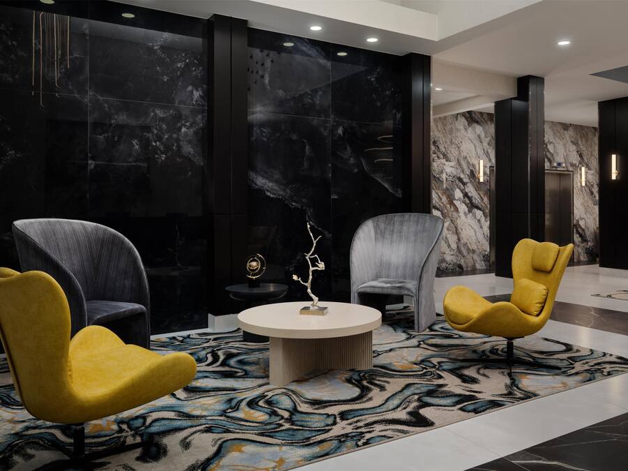 A modern lobby with marble walls, two yellow chairs, a round table, and a patterned carpet.