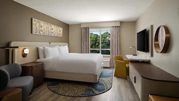 A hotel room with a large bed, a desk, a chair, a TV, and a window with curtains.