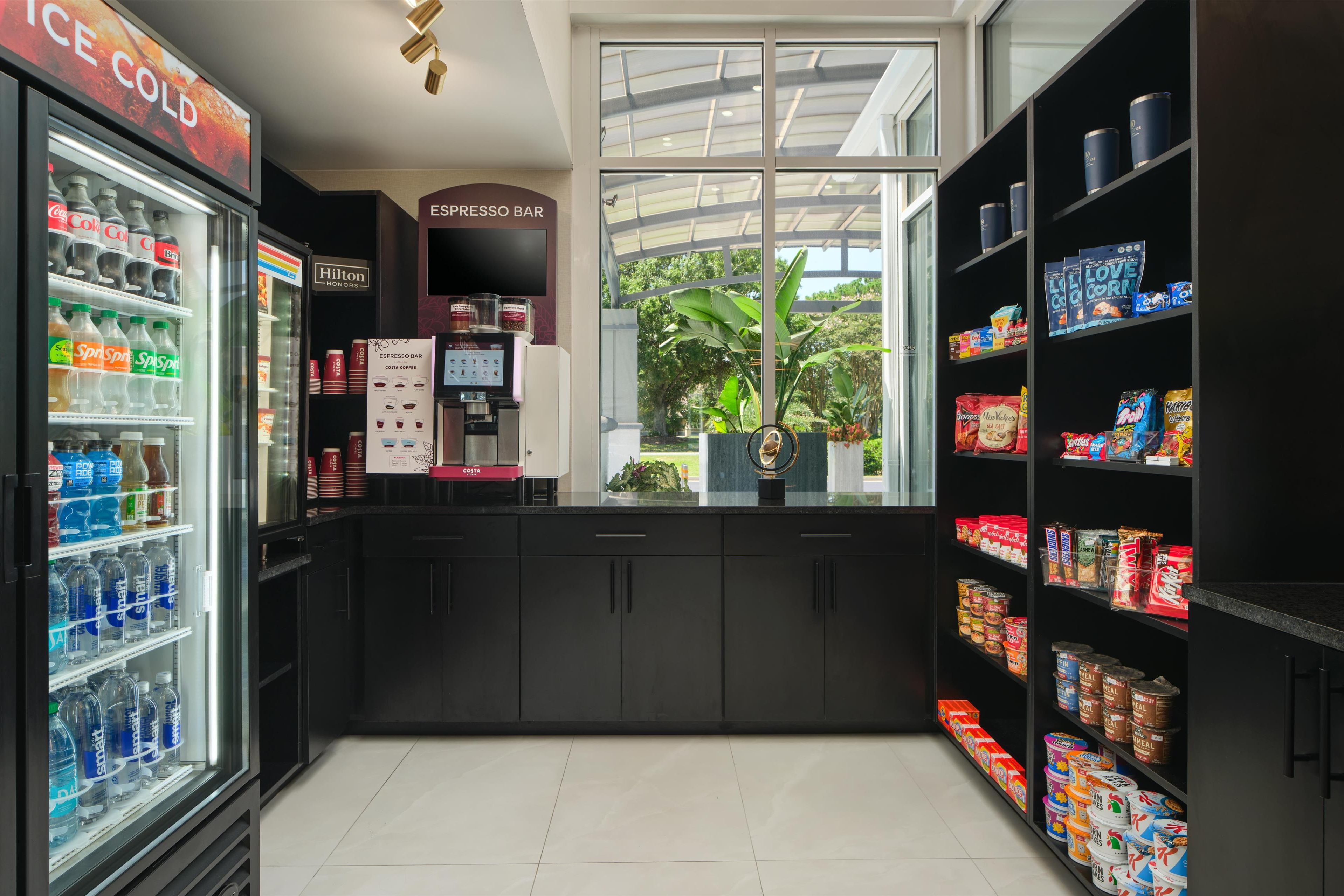 Un hall de hotel con minibar, barra de espresso y estantes llenos de aperitivos y bebidas.