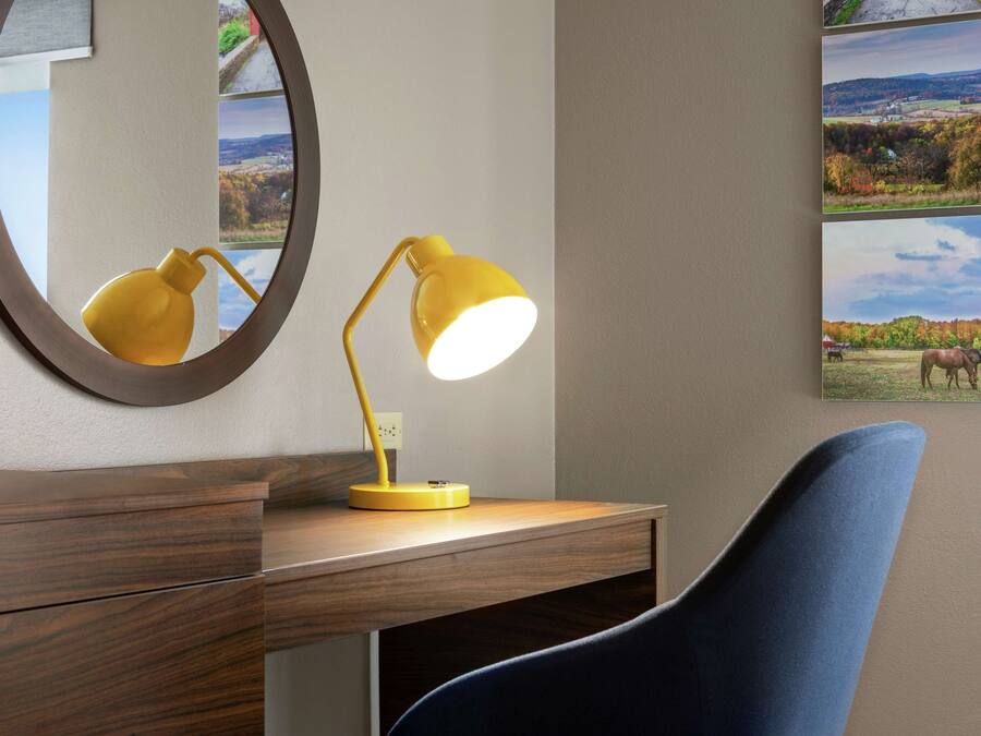 A desk with a yellow desk lamp, a mirror, and a blue chair.