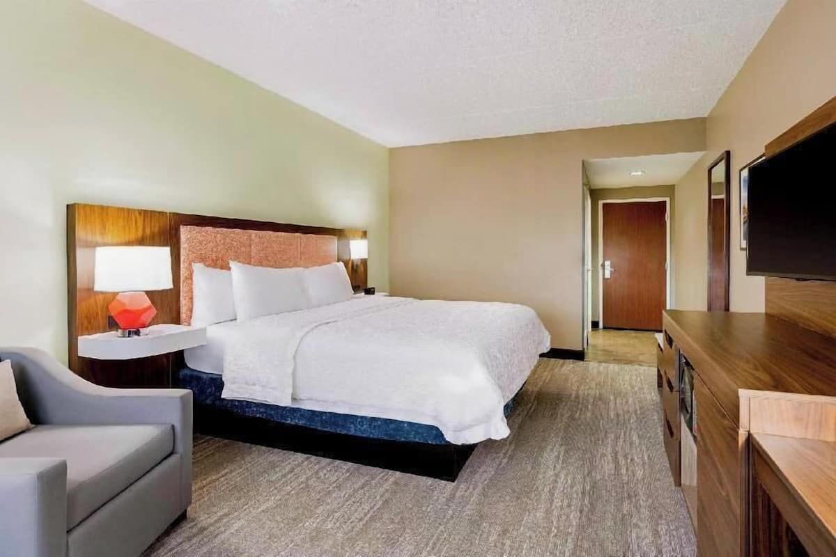 Ein Hotelzimmer mit Bett, Schreibtisch, Sessel, Fernseher und einer Tür zu einem weiteren Raum.