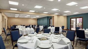 Un salón de banquetes con mesas redondas dispuestas para comer, sillas y un ventanal con vistas.