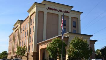Ein Hampton Inn & Suites Hotel mit beige gefasster Fassade, zahlreichen Fenstern und einer Fahnenstange mit der US-amerikanischen Flagge.