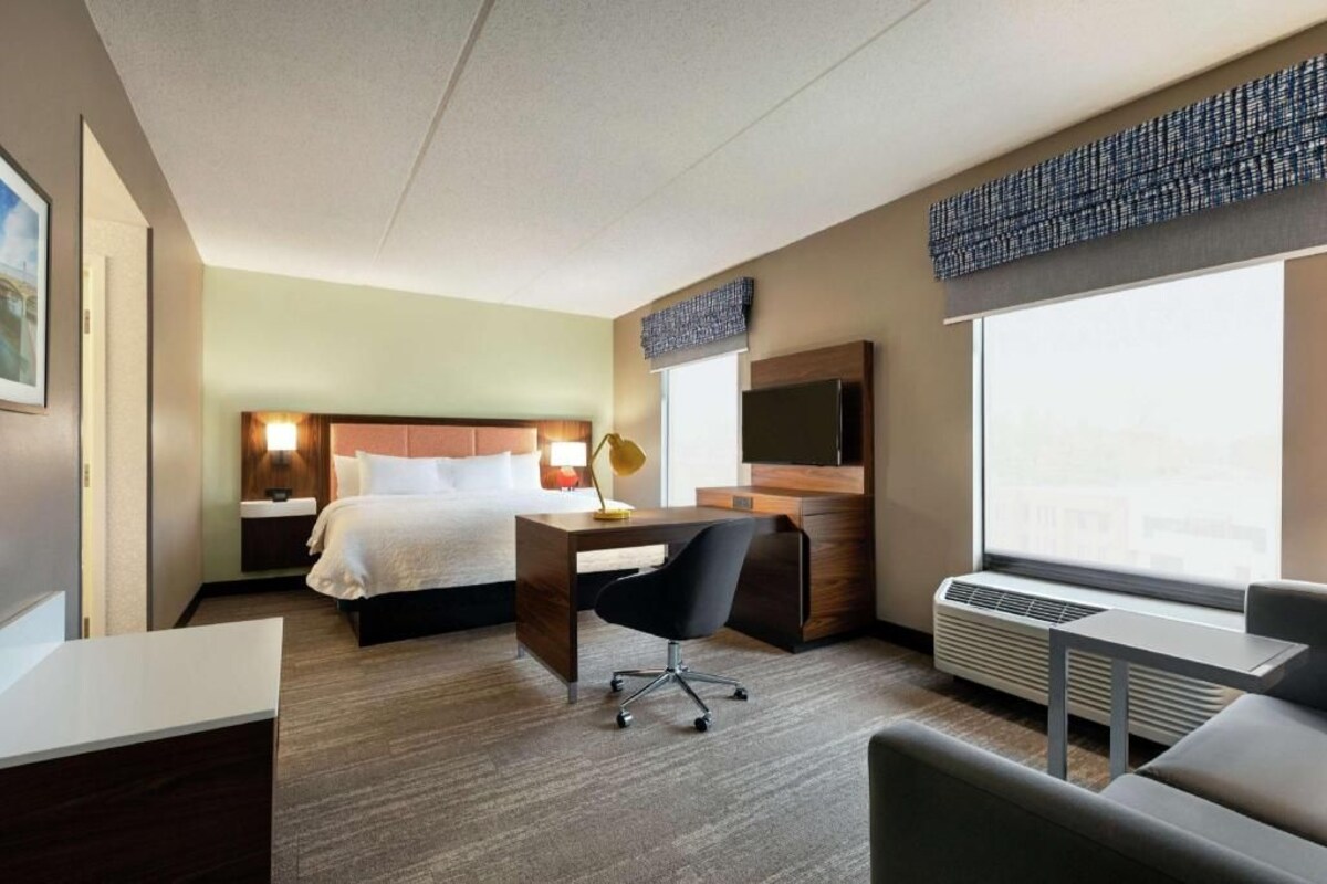 Habitación de hotel con cama, escritorio, silla y un ventanal grande.