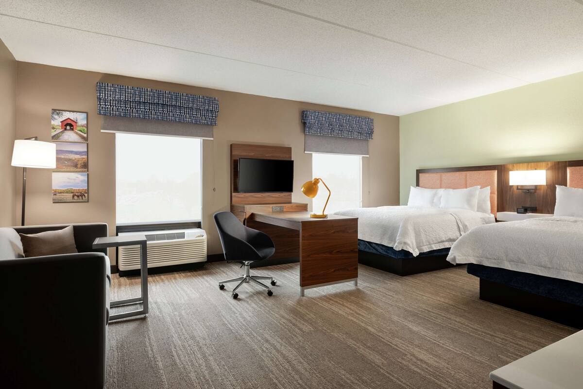 Ein Hotelzimmer mit Schreibtisch, zwei Betten, Fernseher und einem Sessel.