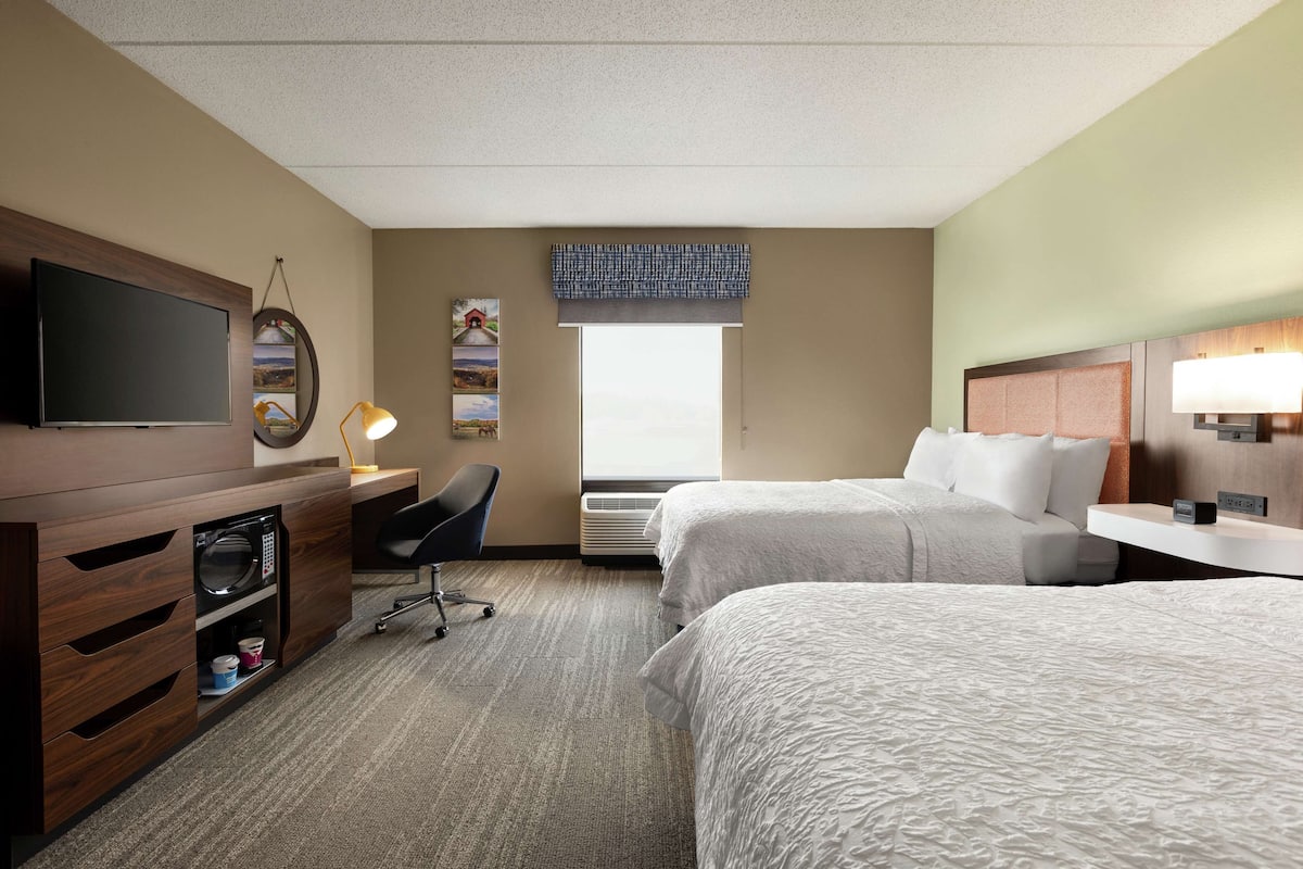 Ein Hotelzimmer mit zwei Betten, einem Fernseher, einem Schreibtisch, einem Stuhl und einem Fenster mit Blick.
