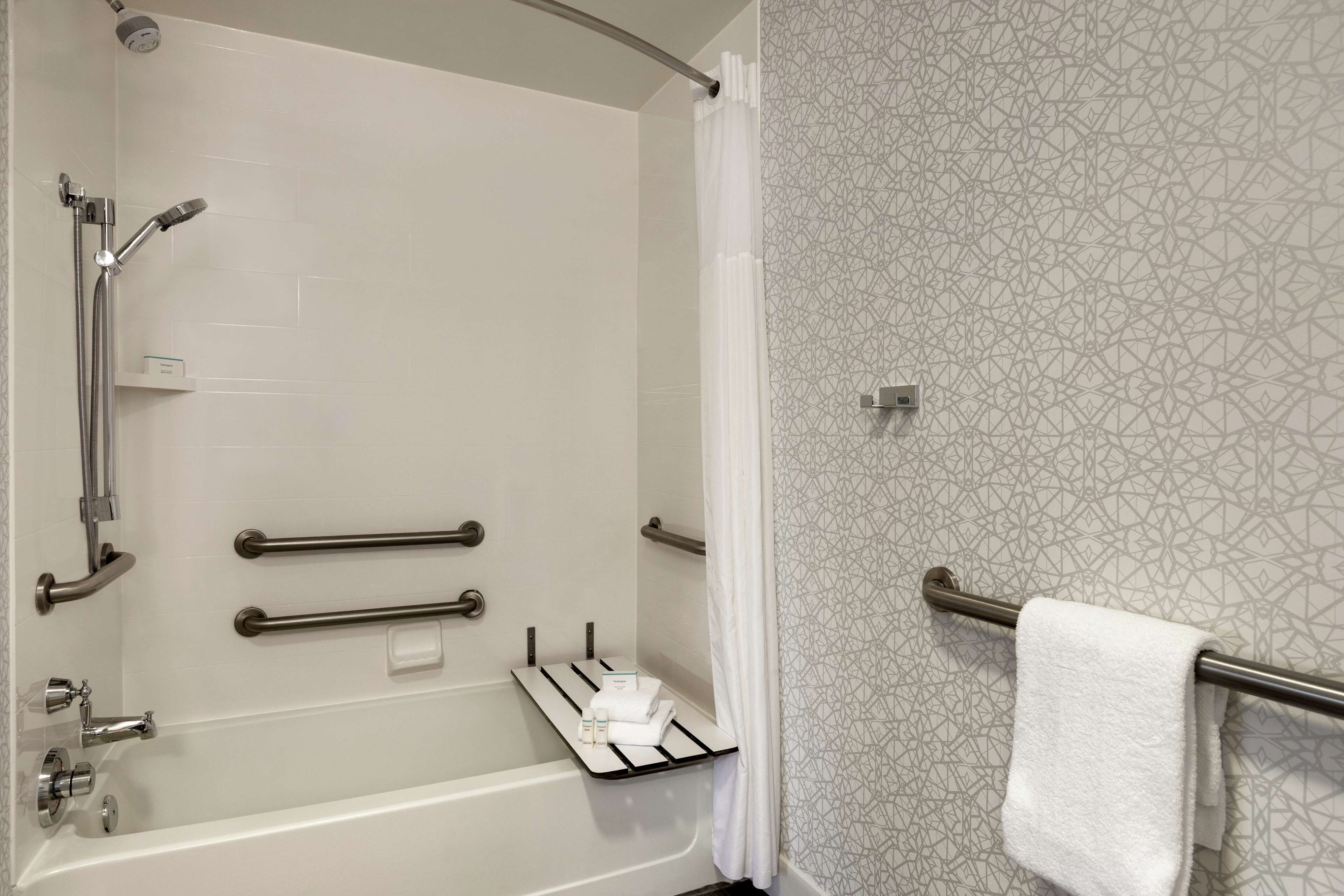 A modern bathroom with a bathtub, shower, and handrails.