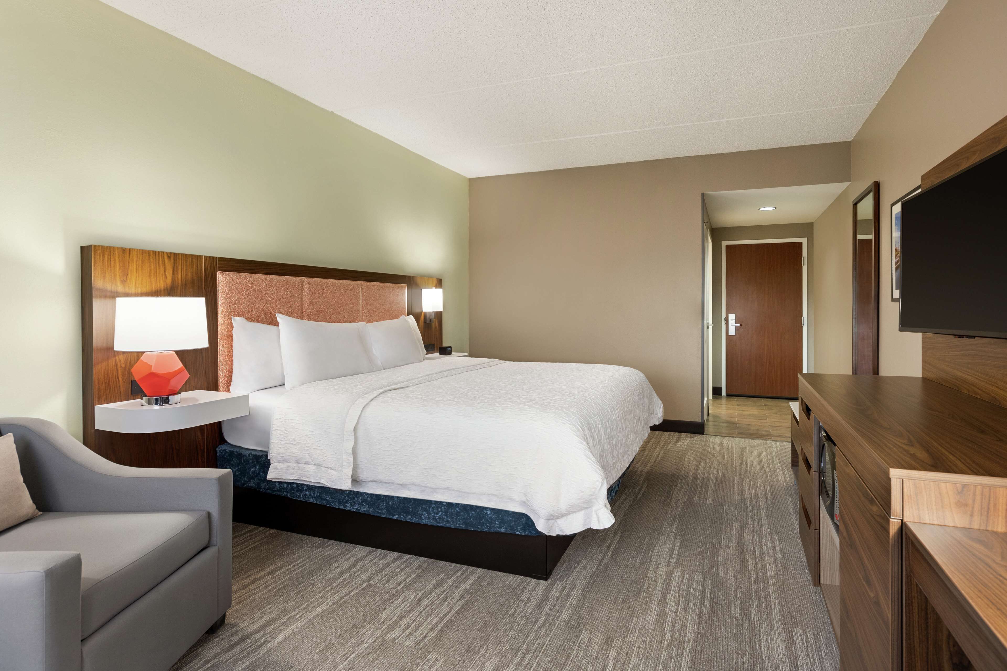 A hotel room with a bed, a desk, a chair, a TV, and a door leading to another room.