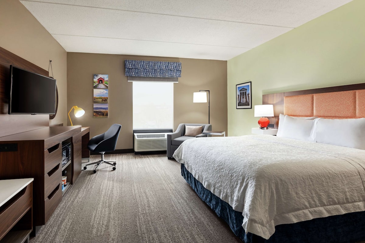 Ein Hotelzimmer mit Bett, Schreibtisch, Stuhl, Fernseher und Kunstwerken an den Wänden.