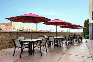 An outdoor patio with tables and chairs, red umbrellas, and a stone wall. - Hampton Inn & Suites Frederick-Fort Detrick (Frederick)