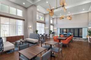 Un hall d’hôtel spacieux doté de plusieurs espaces de détente, notamment des canapés, des tables et des chaises. De grandes fenêtres laissent entrer la lumière naturelle, et le plafond est orné d’un modèle de ventilateur original.
