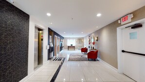 A modern hotel lobby with a clear exit sign, a reception desk, and a seating area with red chairs.