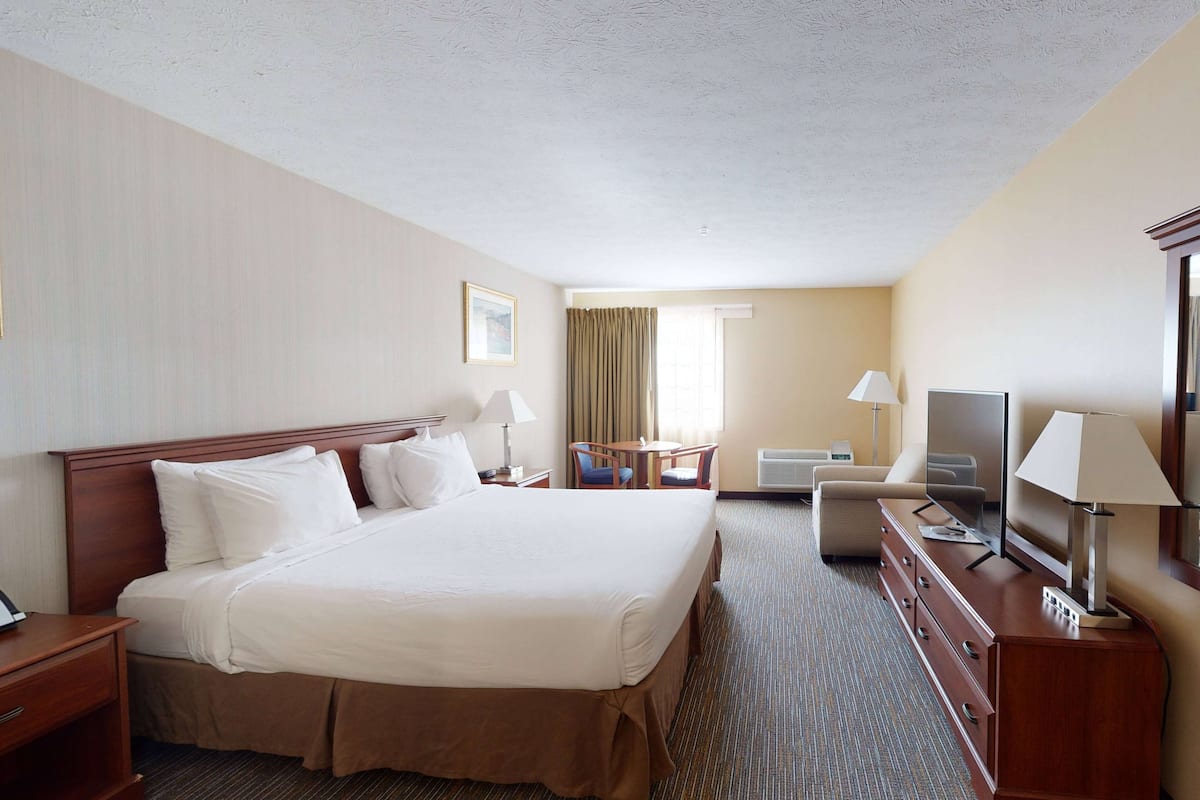A hotel room with a large bed, a desk, a chair, a television, and a dresser.
