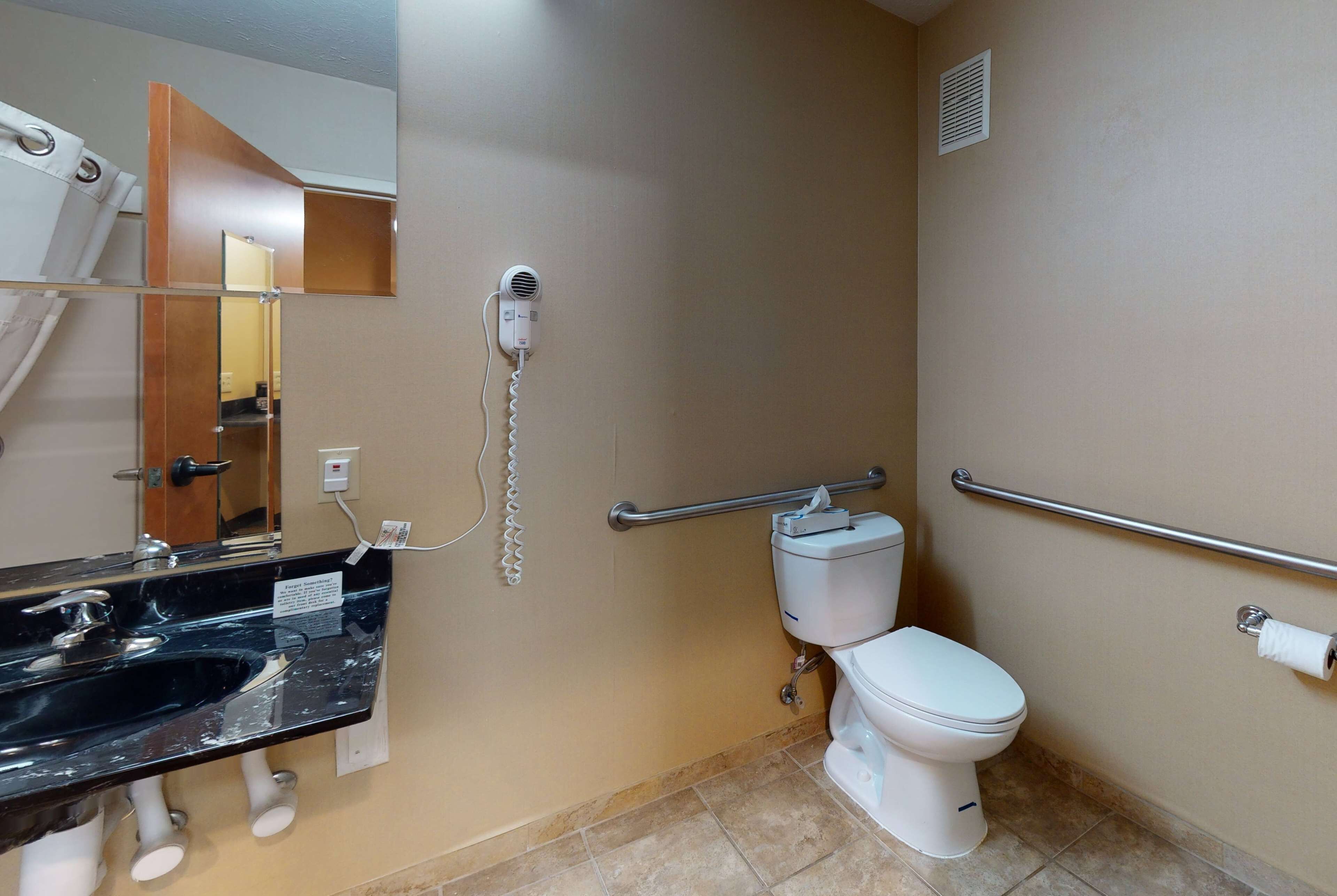 A bathroom with a black sink, a white toilet, a mirror, and a hand dryer.