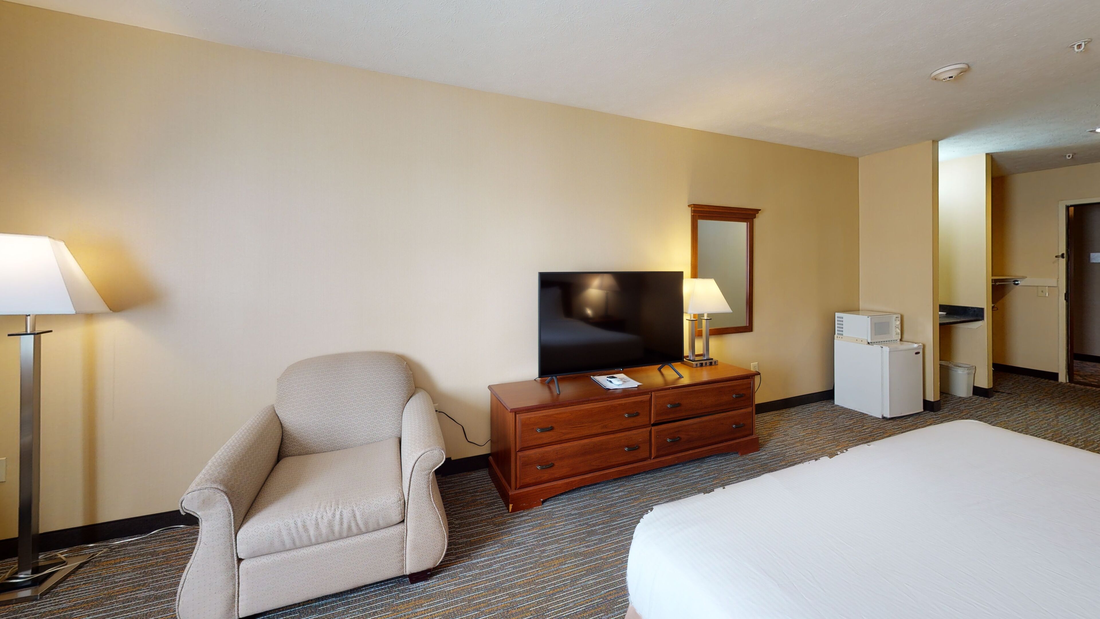 A hotel room with a bed, a chair, a dresser, a television, and a microwave.