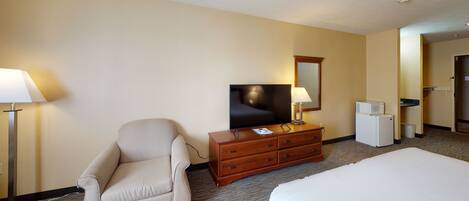 A hotel room with a bed, a chair, a dresser, a television, and a microwave.