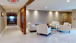 A hotel lobby with a polished tile floor, a reception desk, and seating area with white chairs.