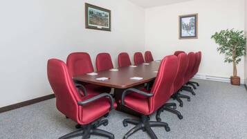 Une salle de conférence avec une table rectangulaire entourée de chaises rouges, des murs blancs et des tableaux encadrés.
