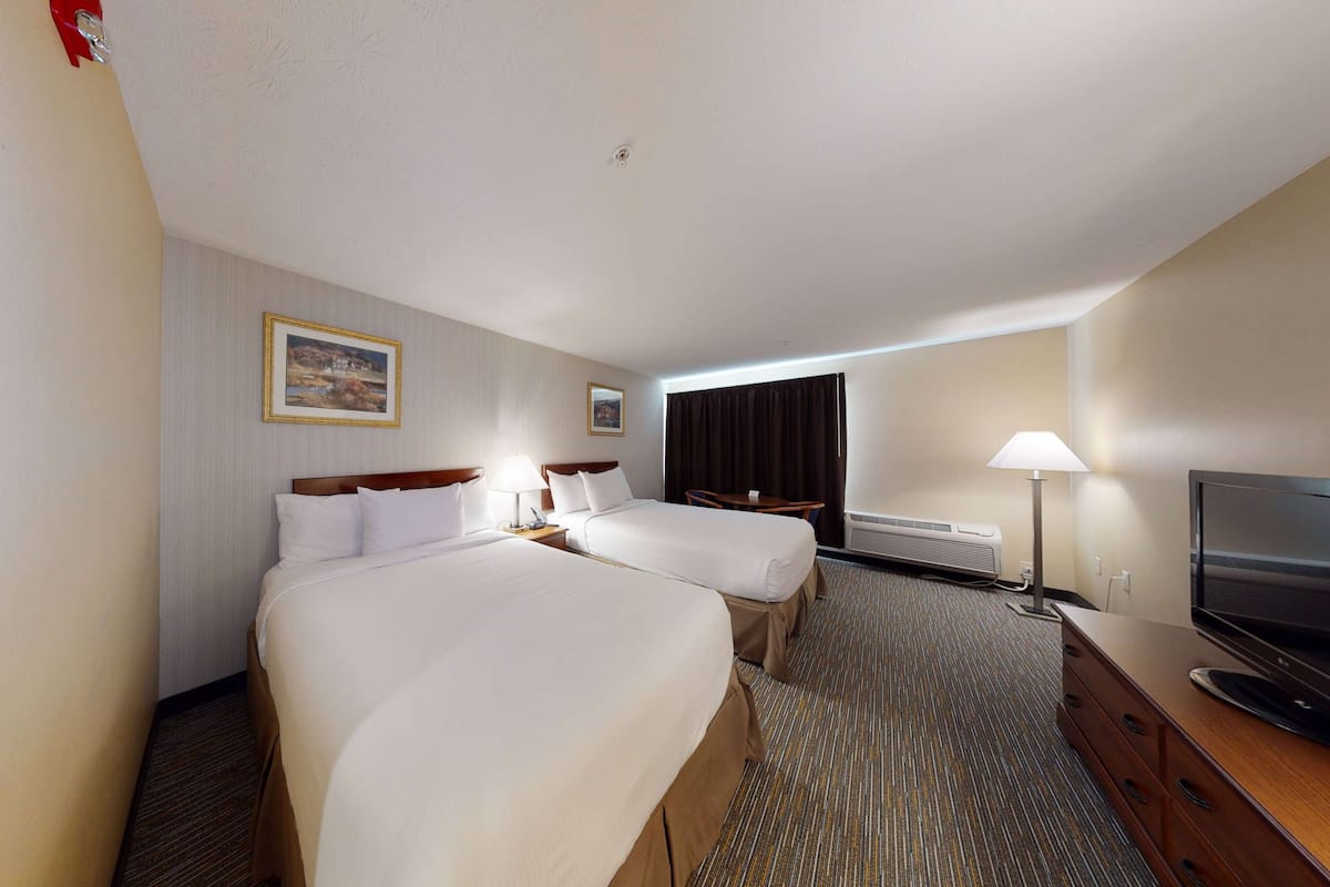 A hotel room with two beds, a TV, a desk, and a lamp.