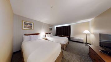 A hotel room with two beds, a TV, a desk, and a lamp.