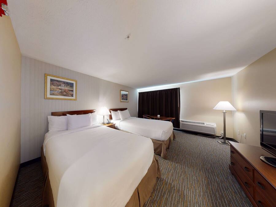 A hotel room with two beds, a TV, a desk, and a lamp.