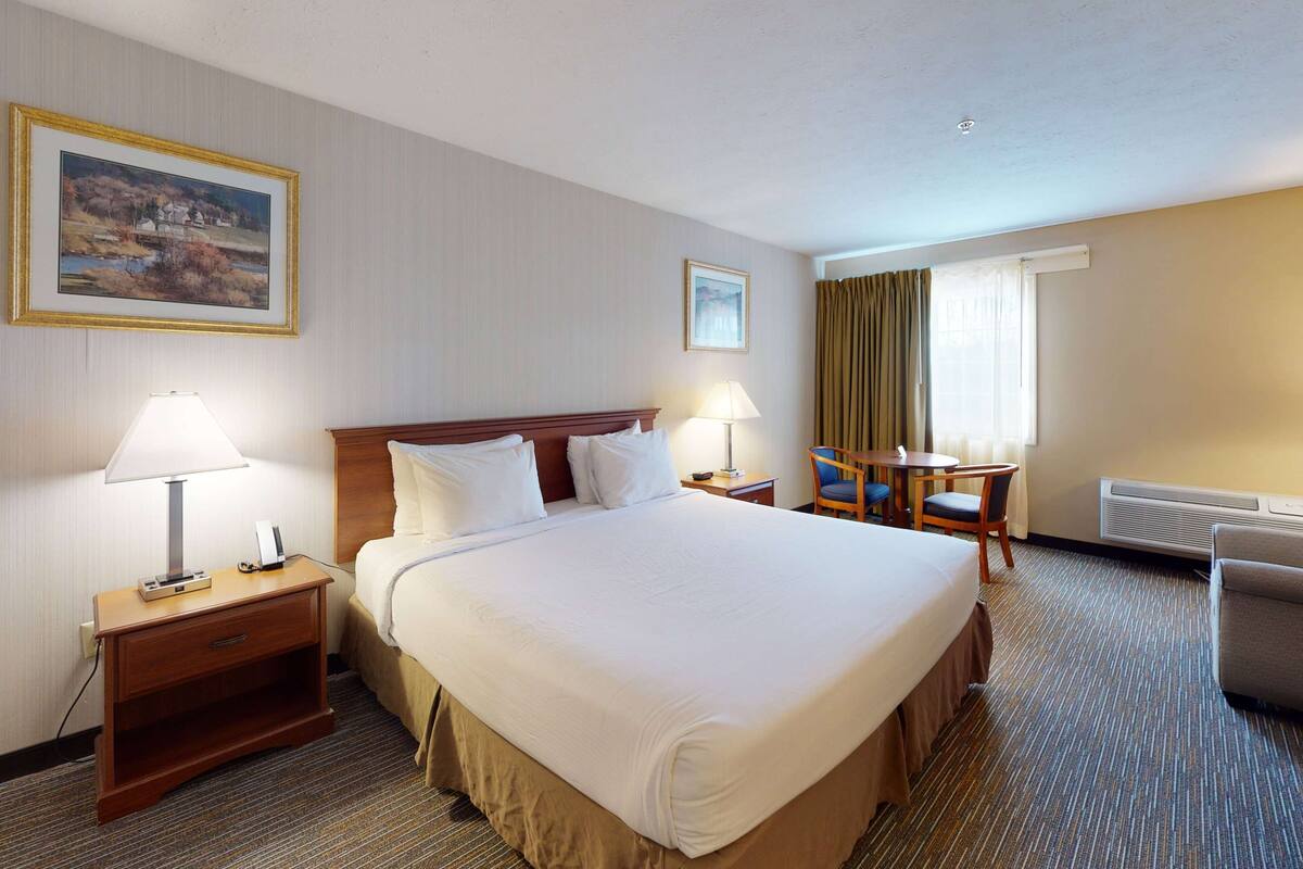 A hotel room with a large bed, two bedside tables with lamps, a desk with a chair, and a window with curtains.