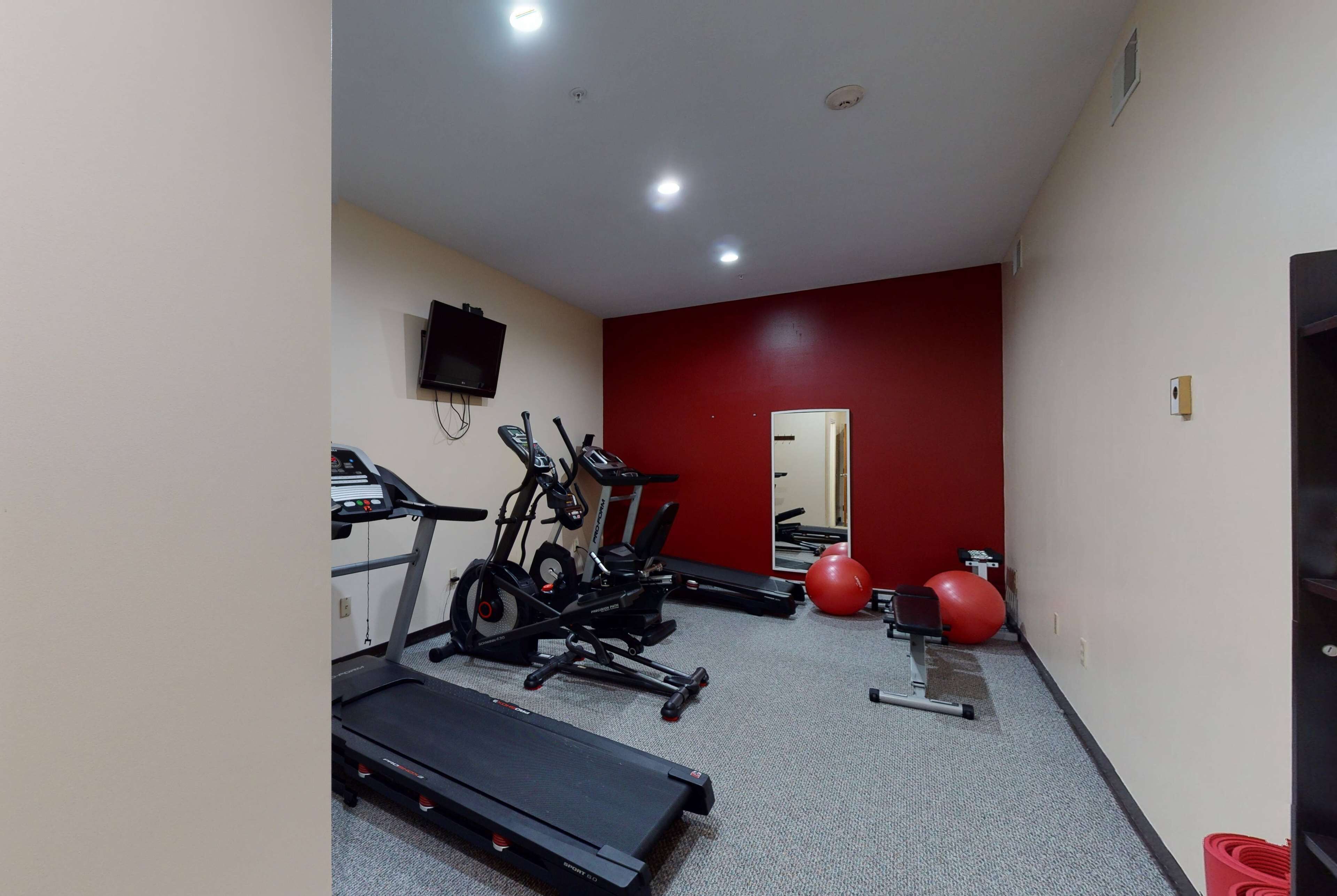 A gym with treadmills, an elliptical, a stationary bike, and a red exercise ball.