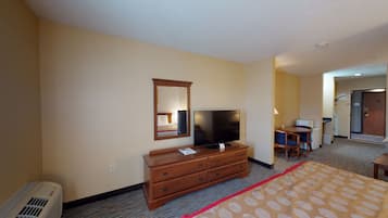 A hotel room with a bed, a dresser, a television, a mirror, and a desk with a chair.