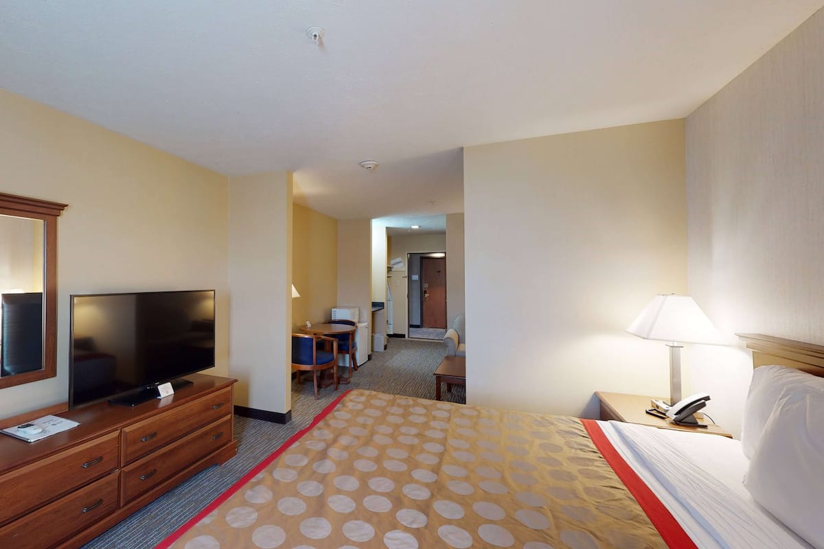 A hotel room with a bed, a TV on a wooden dresser, a desk with a lamp, and a chair.