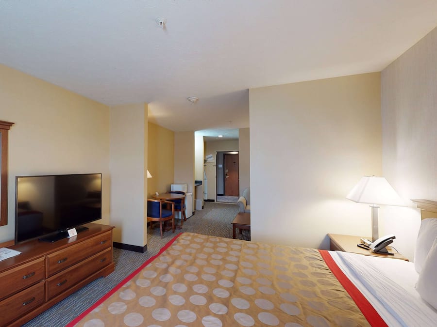 A hotel room with a bed, a TV on a wooden dresser, a desk with a lamp, and a chair.